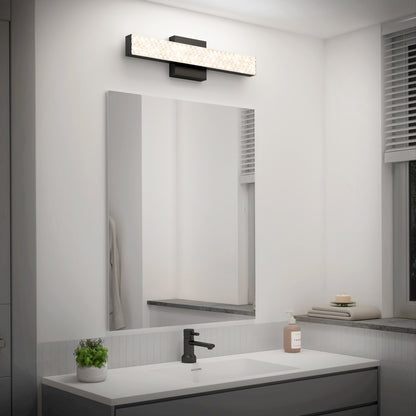 A modern bathroom with a rectangular mirror, black faucet, soap dispenser, and a small potted plant on the sink. Above the mirror is the Artika Adeline modern LED bathroom vanity light 3 CCT. A window with blinds is on the right.