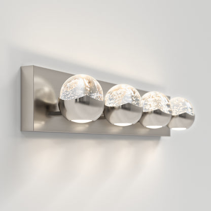 The Artika Oracle 4 light LED bathroom vanity light features four round glass globes, each half clear and half metallic, mounted on a rectangular brushed metal base and illuminated against a white wall.