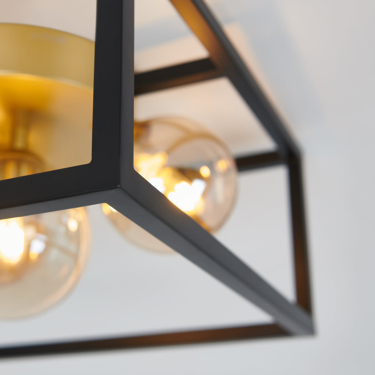 Close-up of a modern ceiling light fixture with exposed bulbs, featuring a black metal geometric frame and gold accents, mounted on a white ceiling.