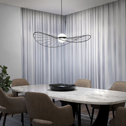 A modern dining room with a white marble oval table, six beige upholstered chairs, a black decorative bowl, and Artika’s Tolena LED pendant light 3 CCT overhead, set against white floor-to-ceiling curtains.