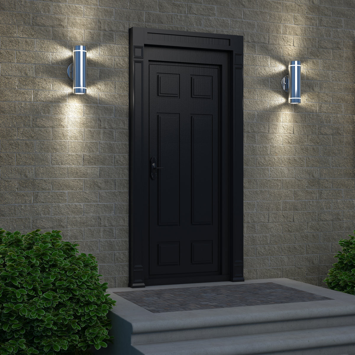 A black paneled door with a handle is set in a brick wall, flanked by two modern wall lights. There are green bushes on either side of the door, and three steps lead up to the entrance.