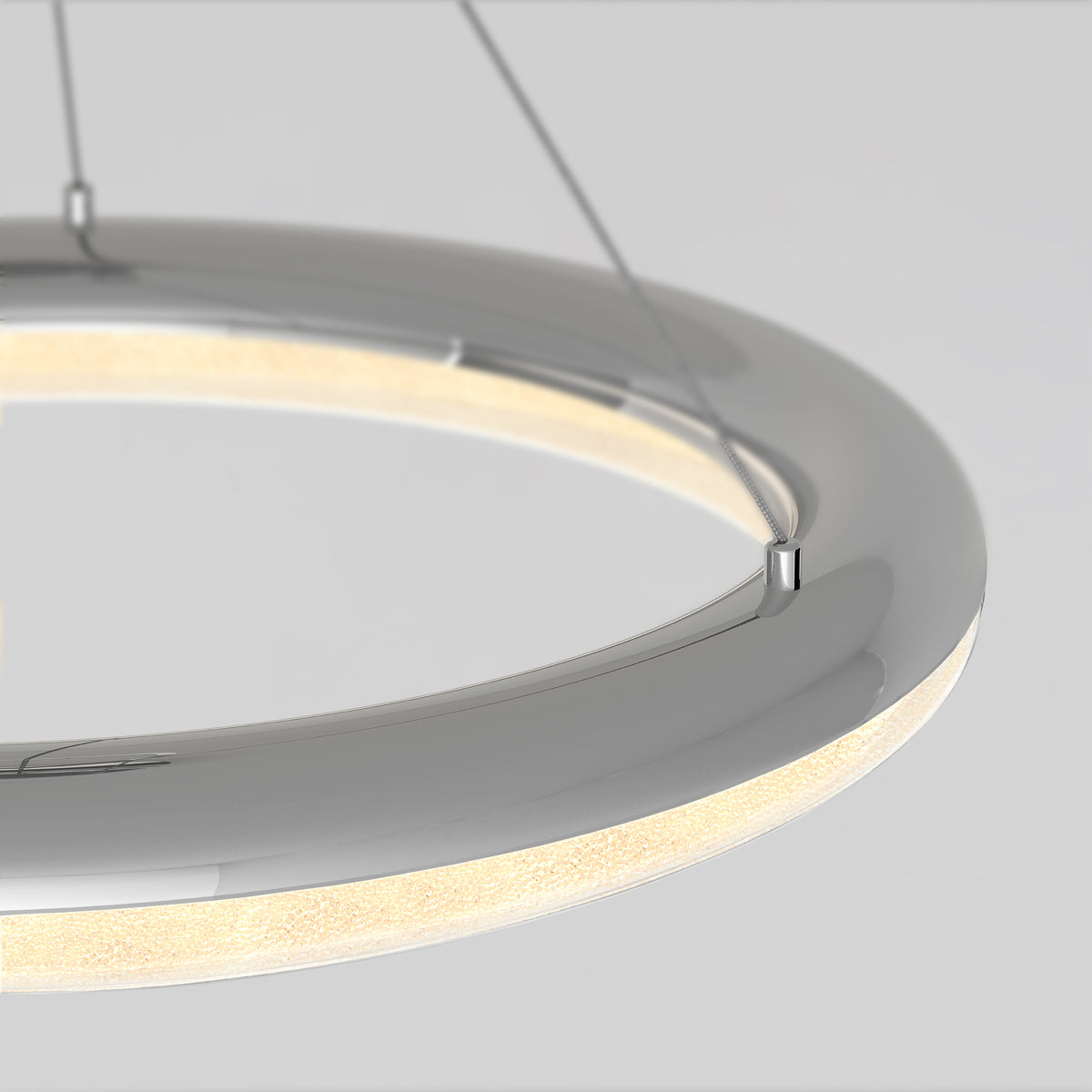A close-up of a modern, circular hanging light fixture with a chrome finish and integrated LED lighting, suspended by thin wires against a plain light background.