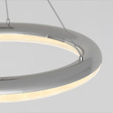A close-up of a modern, circular hanging light fixture with a chrome finish and integrated LED lighting, suspended by thin wires against a plain light background.