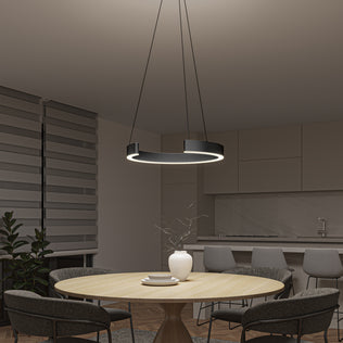 A modern kitchen and dining area with a round wooden table, four gray chairs, a white vase with twigs, and the Artika Vance modern LED pendant light 3 CCT hanging above. Sleek cabinets, a countertop, and a plant complete the background.