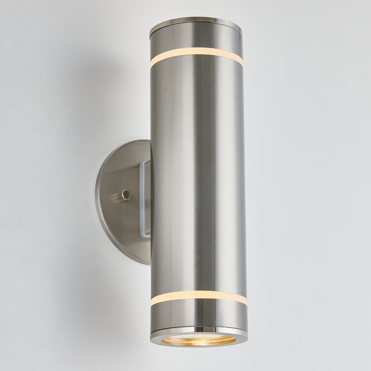 The Artika C7 indoor-outdoor wall light features a modern cylindrical design with a brushed metal finish and round base, emitting a soft glow from both the top and bottom.