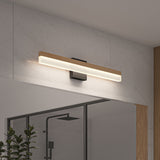 A modern wall-mounted light fixture with a wooden accent and frosted panel is installed above a bathroom mirror on a light gray tile wall. A shower and a plant are partially visible in the foreground.