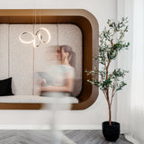 A modern interior with a built-in cushioned bench, a black pillow, a contemporary light fixture, and a potted plant. A woman in motion appears blurred as she walks past the seating area.