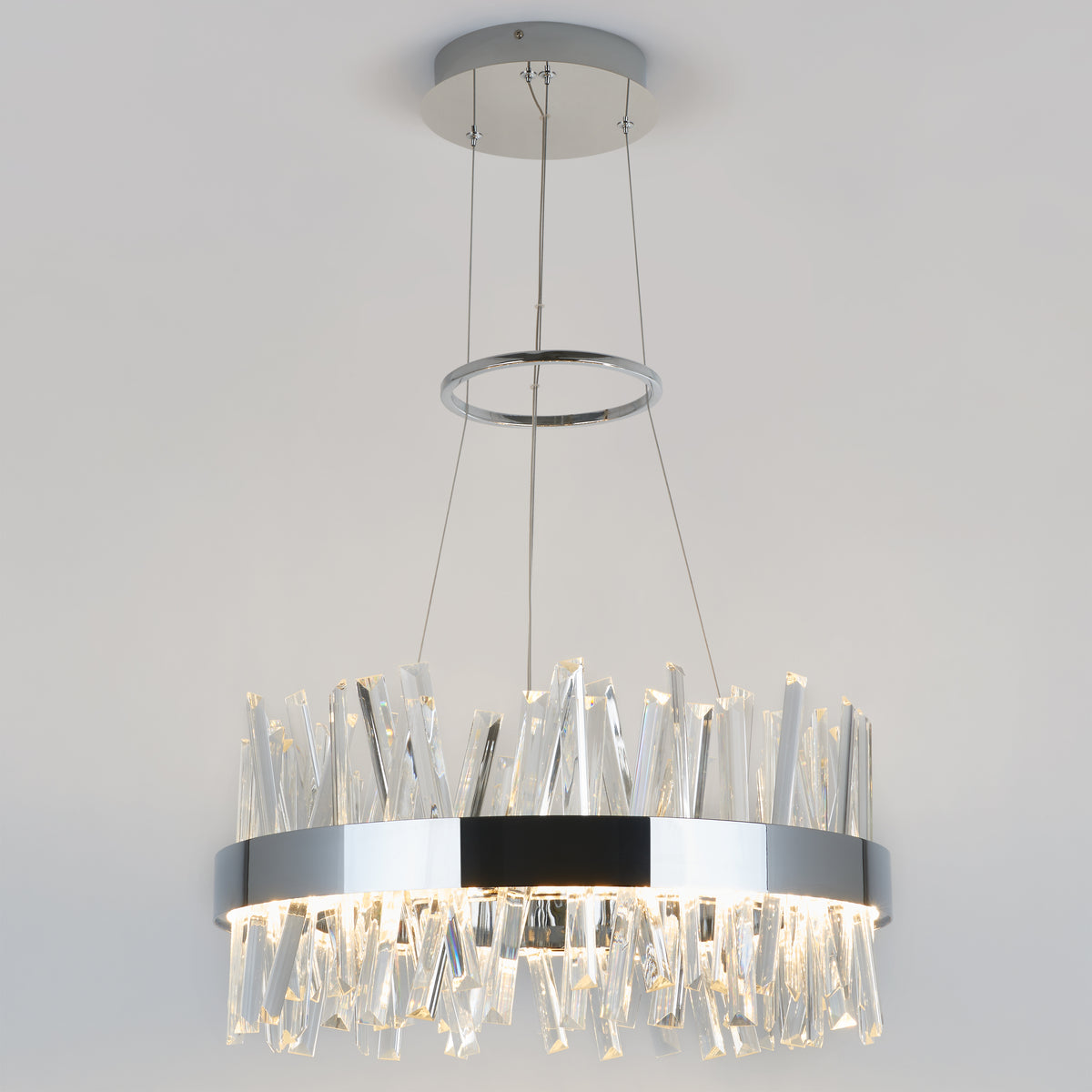 Modern chandelier with a circular chrome frame, featuring multiple clear, jagged crystal rods hanging down, suspended from the ceiling by three thin cables against a plain light background.