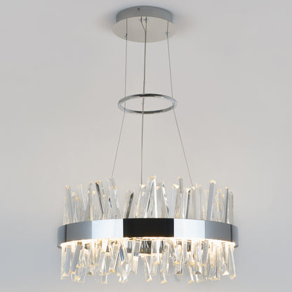 The Artika Enchanted LED pendant light features a circular chrome frame suspended by cables, with irregular clear glass prisms that emit soft white light, creating a modern look against any white ceiling.