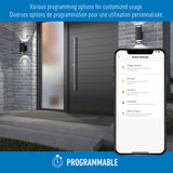 A smartphone displays smart home settings in front of a modern house entrance at night. The image highlights programmable features for customized usage in English and French.