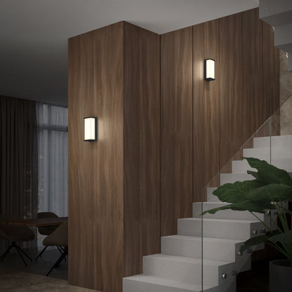 Modern interior featuring a wooden-paneled wall, white staircase with glass railing, two Artika Faro modern LED indoor-outdoor wall lights (3 CCT), a large plant, and a dining area visible through tall windows in the background.