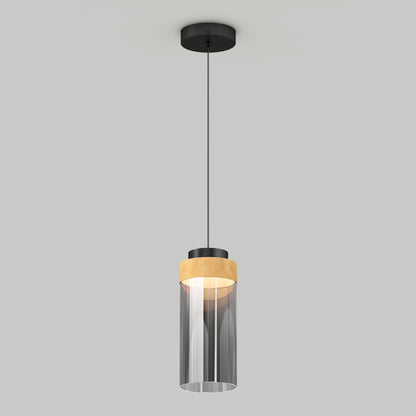 The Artika Hanson 1-light LED pendant 5 CCT features a black ceiling mount, black cord, cylindrical glass shade with a wooden accent on top, and emits a soft glow when illuminated.