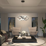 A modern living room with two beige armchairs, a dark sofa, a black coffee table with books and flowers, a patterned rug, and a futuristic chandelier. Large windows and indoor plants complete the elegant space.