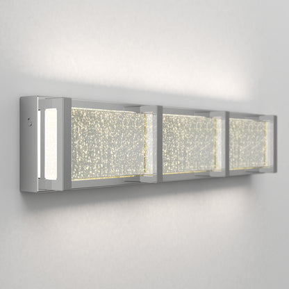 The Artika Subway Essence 3 LED bathroom vanity light features three rectangular frosted glass panels with a speckled pattern, emits soft white light, and is framed in brushed metal for a modern wall-mounted look.