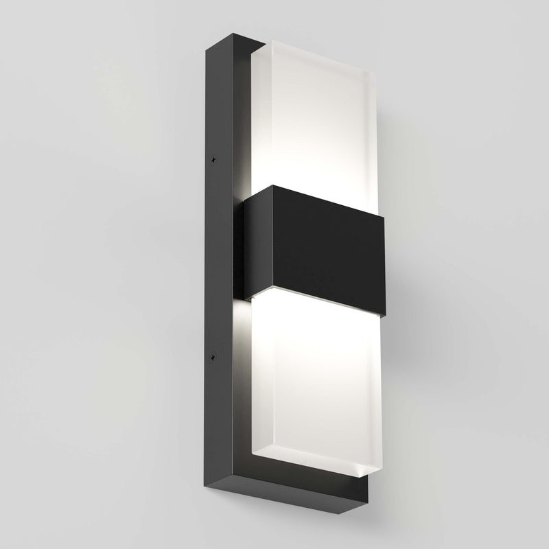 The Artika Mazza Frosted indoor-outdoor LED wall light features a sleek rectangular black metal frame with two frosted glass panels, casting a soft glow on a light gray wall.