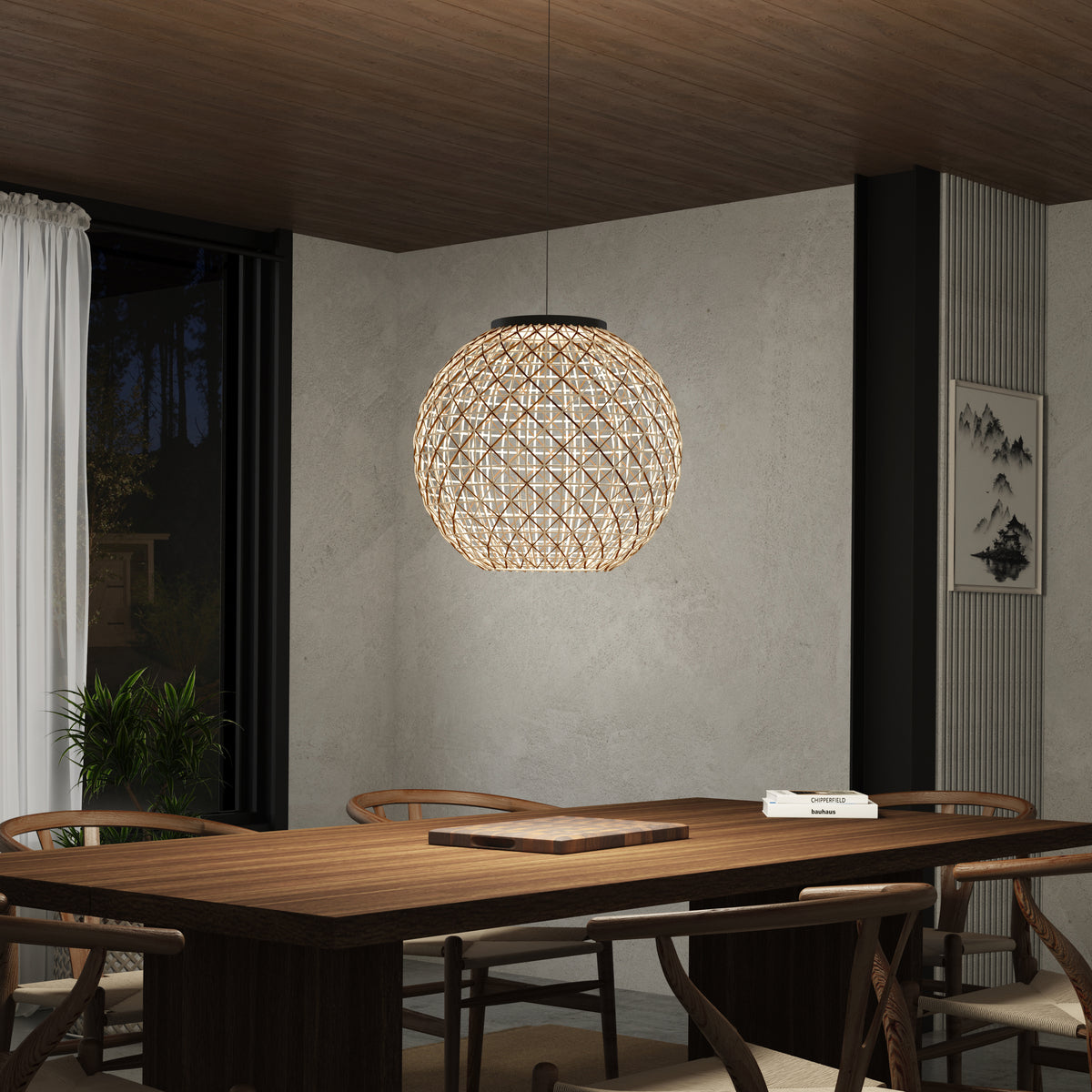 A modern dining room with a wooden table, chairs, and a spherical, woven pendant light hanging from the ceiling. The space features neutral walls, a plant, a window with white curtains, and a few books on the table.