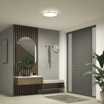 Modern entryway with a gray door, an Artika Hemisphere 15 in. LED flush mount light (5 CCT adjustable), an oval mirror above a floating wooden shelf, bench, scarf and hat on wall hooks, and a large potted plant by the door.