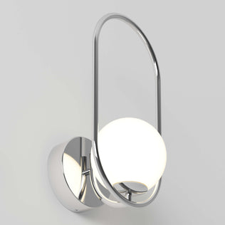 The Artika Bloom LED Sconce 3 CCT features a chrome finish, round base, and glowing white spherical bulb within an oval metal frame, shown against a plain light gray background.
