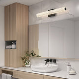 Modern bathroom with a round white vessel sink, black faucet, light wood cabinetry, a large mirror, glass light fixture above, and small plant on the counter. White and marble surfaces create a clean, minimalist look.