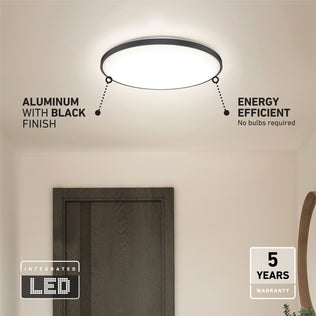 The Artika Europa 21 in. LED modern flush mount light with remote, featuring a black aluminum finish, is mounted above a dark wooden door. It offers energy efficiency, integrated LED technology, no bulb changes needed, and a 5-year warranty.