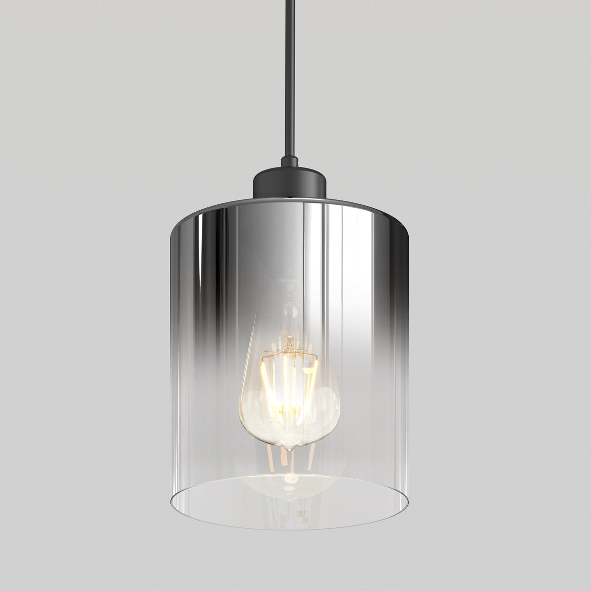 A modern pendant light with a clear cylindrical glass shade and a visible glowing bulb, suspended from a black cord against a plain light gray background.