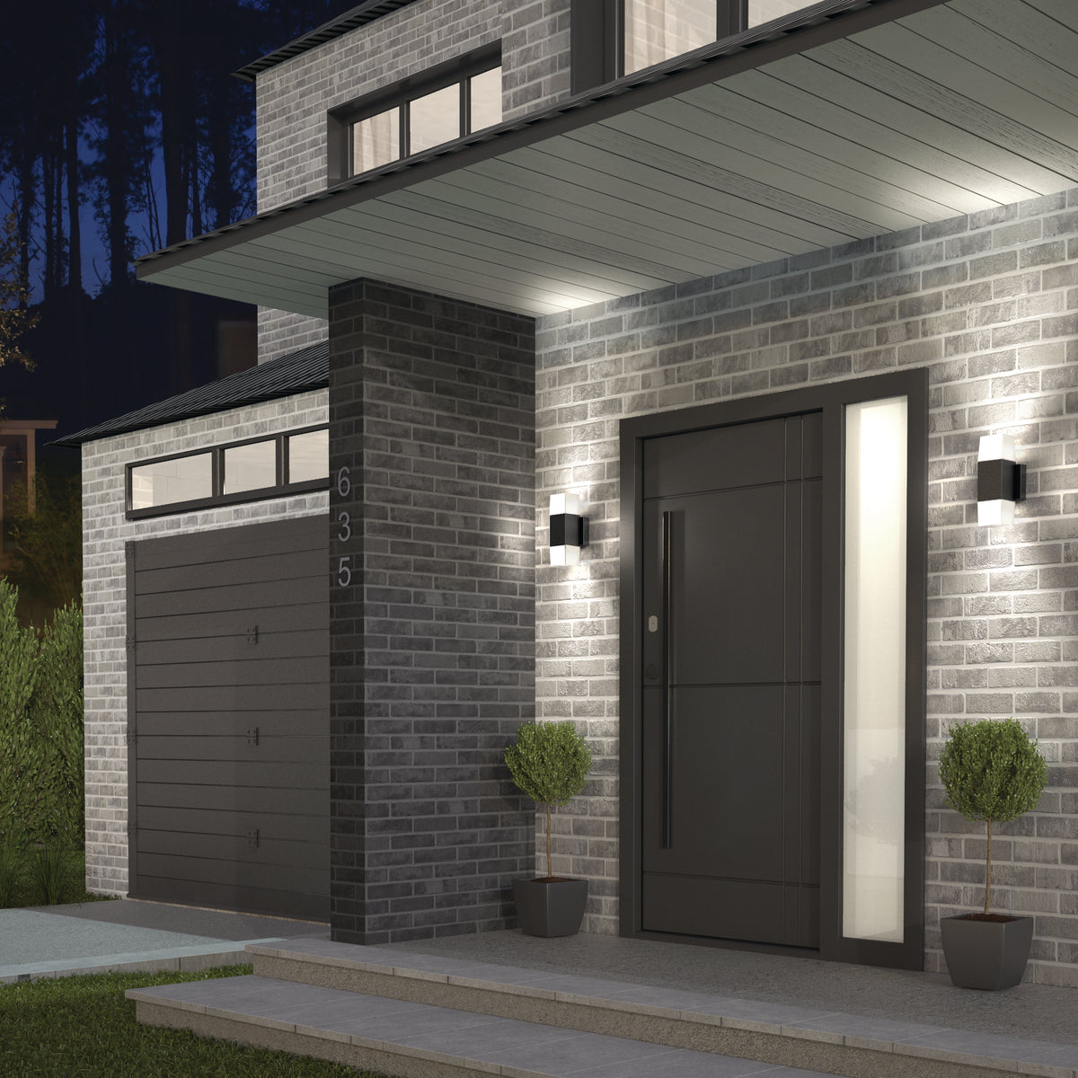 Modern home exterior at dusk with gray brick walls, black front door with a vertical glass panel, black garage door, two potted topiary plants by the entrance, and wall-mounted lights illuminating the porch.