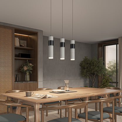 Modern dining room with a wooden table and six chairs, Artika’s Barden 3-light LED pendant light above, built-in shelves with decor, a large potted plant, and natural light from a window on the right.