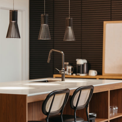 A modern kitchen with a wooden island, two bar stools, a built-in sink, and three Artika Kiyo modern LED pendant 3 CCT lights overhead. Dark textured walls and a coffee maker feature in the background.