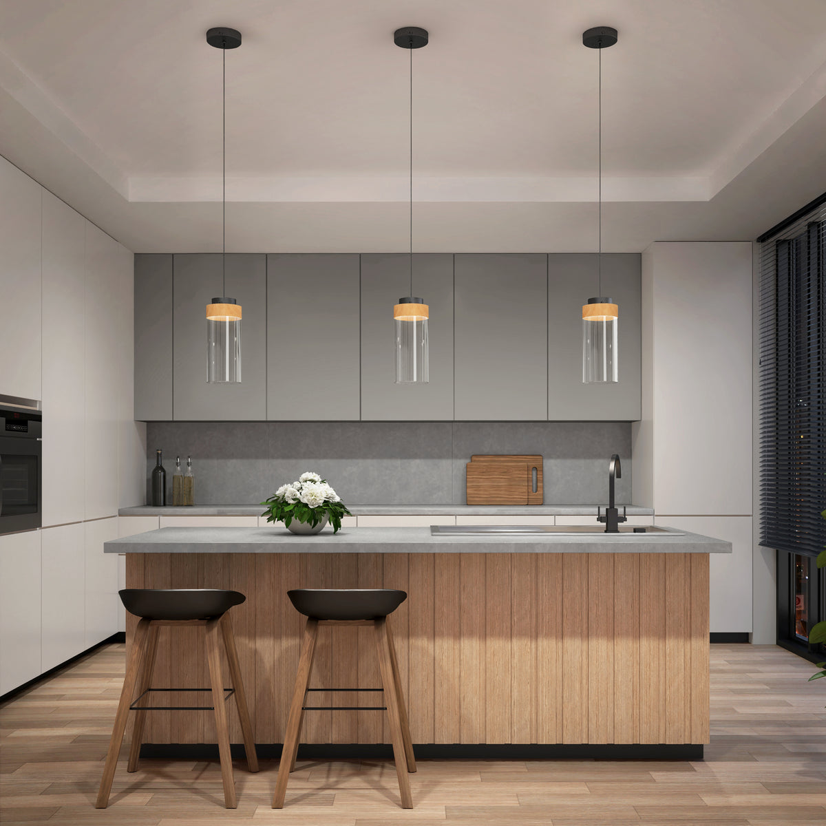 Modern kitchen with light wood and gray cabinets, a central island with two dark stools, three hanging glass pendant lights, a sink, cutting board, and a vase of white flowers, with natural light coming from large windows.