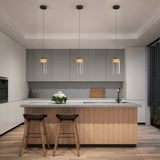 Modern kitchen with light wood and gray cabinets, a central island with two dark stools, three hanging glass pendant lights, a sink, cutting board, and a vase of white flowers, with natural light coming from large windows.