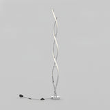 A modern floor lamp with two intertwined, twisting metal rods, one of which emits light. The lamp stands on a small rectangular base with a visible power cord and foot switch, set against a plain gray background.