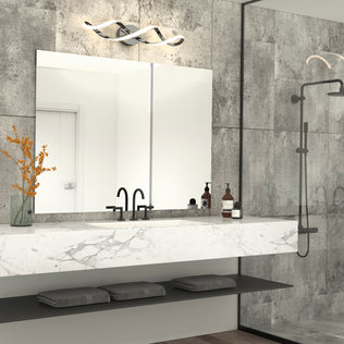 Modern bathroom with a large mirror, marble countertop, black faucet, decorative vase with orange flowers, toiletries, and folded gray towels on a below-shelf. Gray tiled walls, Artika Swirl modern LED vanity light, and glass shower are visible.