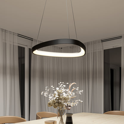 The Artika Bjorn modern LED pendant light 5 CCT, with its sleek oval shape and black finish, hangs above a light wooden table adorned with dried flowers. Sheer white curtains cover large windows in the softly lit room.