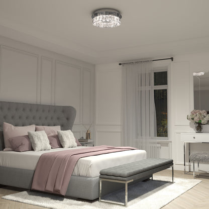 A modern bedroom with a tufted gray bed, white and blush bedding, a gray bench, sheer curtains, a white vanity with flowers, and the Artika Celebrity LED flush mount light on the ceiling. The room features elegant neutral decor.