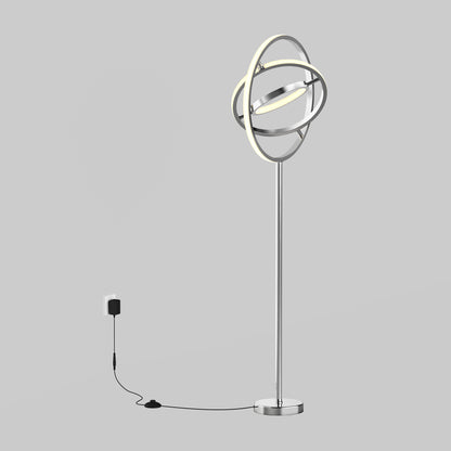 The Artika Pivot modern LED floor lamp 3 CCT features interlocking circular LED rings, a chrome base, and a black power cord for wall outlet connection, set against a plain gray background.