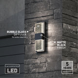 A modern outdoor wall light with a bubble glass diffuser and matte black finish is mounted on a dark stone wall. Text highlights integrated LED and a 5-year warranty.