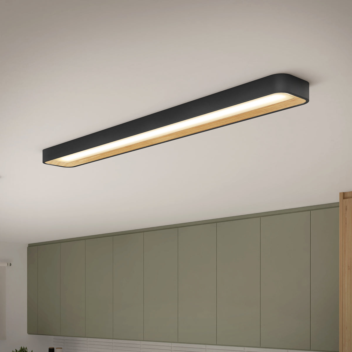 A rectangular, modern ceiling light fixture with a black frame and warm light is mounted above sage green kitchen cabinets and a white tiled backsplash.
