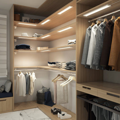 The Artika Maestro under cabinet LED light 3CCT brightens a modern walk-in closet, illuminating wooden shelves, hanging clothes, and storage baskets for a tidy, spacious look with neatly organized coats, shirts, and jackets.