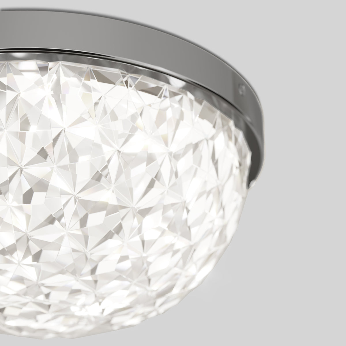 A close-up of a modern ceiling light fixture with a geometric, faceted glass cover and a sleek metal trim, emitting bright white light. The background is a plain light gray.