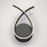 A modern, minimalist LED desk lamp with two black curved arms crossing at the top, each lined with a glowing light strip, mounted on a round black base against a plain white background.