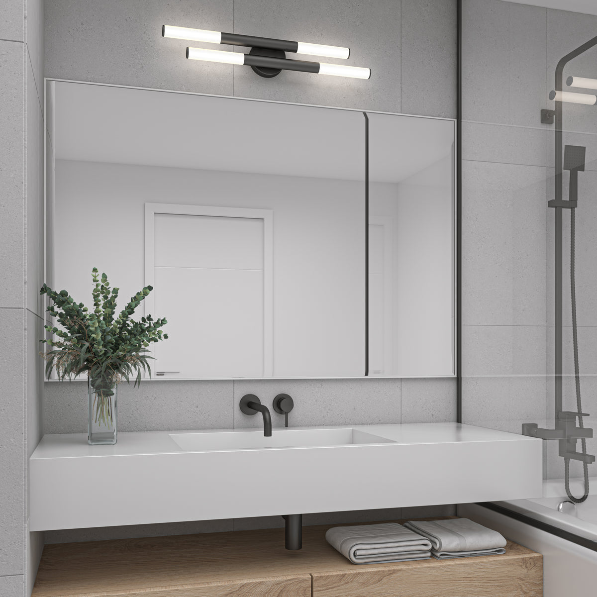 A modern bathroom with a large mirror above a white double sink, black fixtures, a vase with green foliage, folded towels on a wooden shelf, and a wall-mounted light fixture above the mirror.