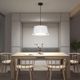 A modern dining area with a wooden table, four matching chairs, a grey cushioned bench, a white pendant light above, and a small vase with branches as the centerpiece. Neutral tones create a minimalist atmosphere.