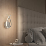 A modern bedroom with a tufted headboard, gray bedding, a geometric-patterned pillow, and a unique loop-shaped wall lamp above a nightstand with a coffee cup, book, and pen.