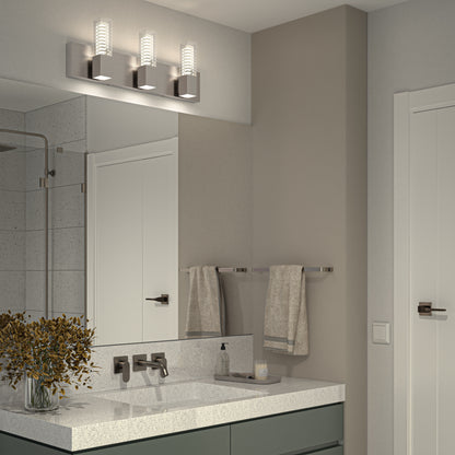 Modern bathroom with a large mirror above a white countertop, wall-mounted faucet, beige towels on racks, and Artikas Hologram LED modern bathroom vanity light 5 CCT above the mirror. A vase with greenery sits on the counter.