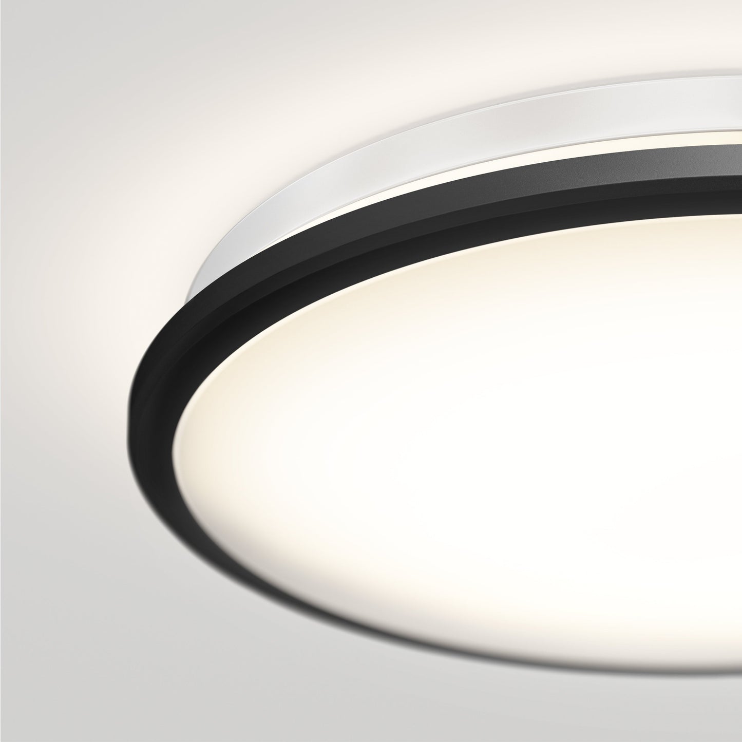 A close-up of the Artika-CAN-dev Vera 13 in. LED modern flush mount light features a matte black finish, silver rim, glowing white center emitting 200 lumens, and is mounted on a white ceiling.