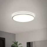 A modern, round ceiling light fixture emits a bright white glow in a minimalistic room with white walls and a small leafy plant visible in one corner.