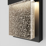 A modern wall sconce with a rectangular, bubble-filled glass panel illuminated from behind, mounted on a black metal frame.