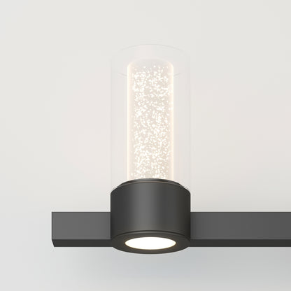 The Artika Novello modern LED bathroom vanity light features a black rectangular base and a cylindrical bubble glass shade, casting a soft glow against a plain white background.