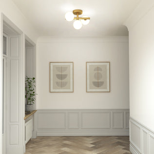 A bright hallway features light gray wainscoting, herringbone wood floors, two minimalist wall prints, and a potted plant on the windowsill, illuminated by the Artika Bloom modern mid-century LED flush mount light 5 CCT.
