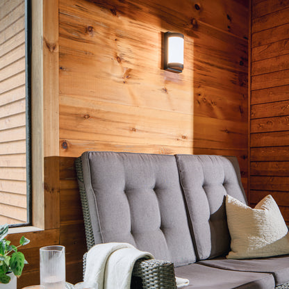 Cozy patio with gray seating, a white pillow, throw blanket, and Artika Fogo modern LED wall light on wood paneling near a window.